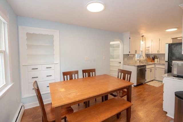 dining space featuring arched walkways, a baseboard radiator, and light wood-type flooring