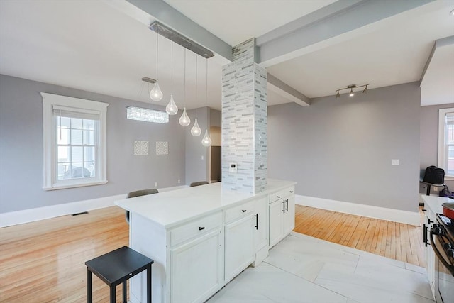 kitchen featuring baseboards, visible vents, decorative columns, white cabinets, and beamed ceiling