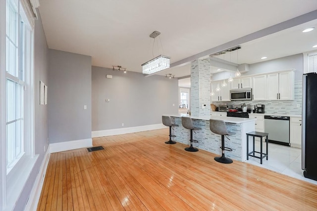 kitchen with a kitchen breakfast bar, visible vents, white cabinets, and stainless steel appliances