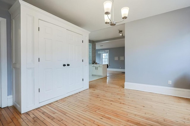 spare room with light wood finished floors, baseboards, and an inviting chandelier