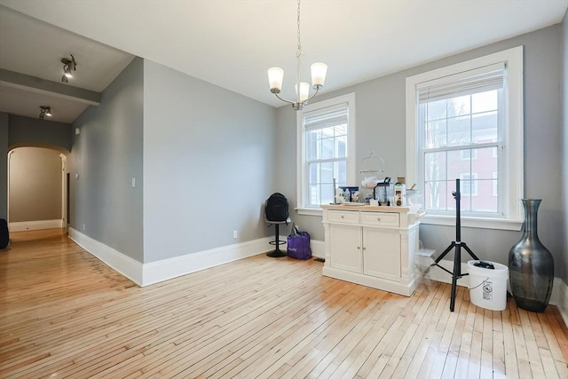 misc room with arched walkways, light wood-style flooring, an inviting chandelier, and baseboards