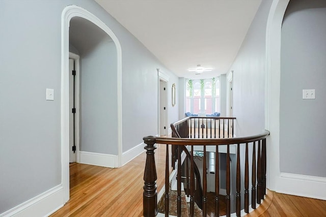 hallway with an upstairs landing, baseboards, arched walkways, and light wood-style flooring