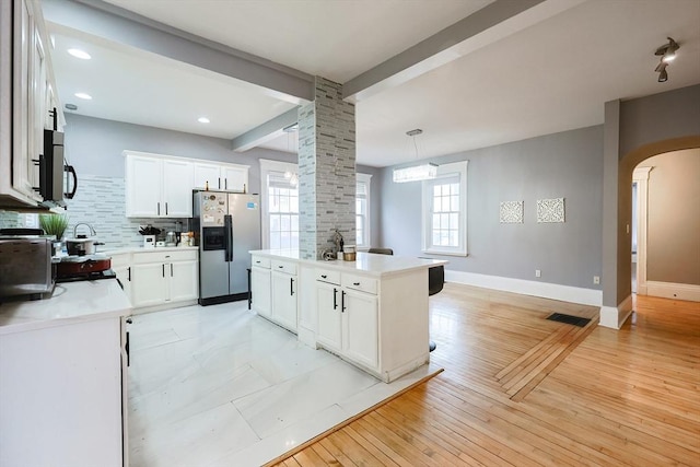 kitchen featuring baseboards, beam ceiling, decorative backsplash, stainless steel refrigerator with ice dispenser, and arched walkways