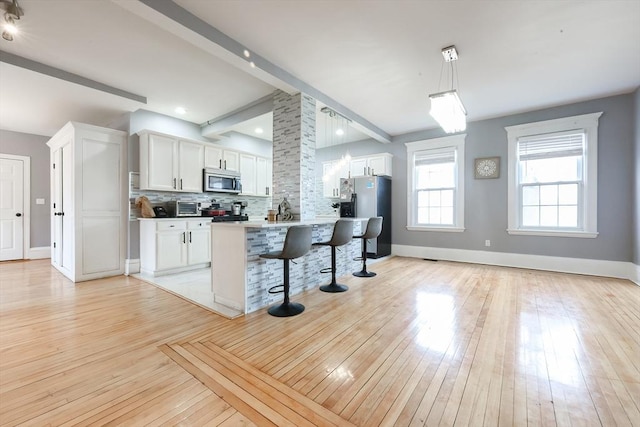 kitchen with beamed ceiling, a breakfast bar area, decorative backsplash, light wood-style flooring, and stainless steel appliances