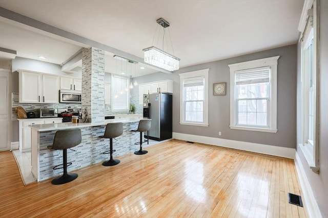 kitchen featuring visible vents, decorative backsplash, white cabinets, appliances with stainless steel finishes, and a kitchen breakfast bar