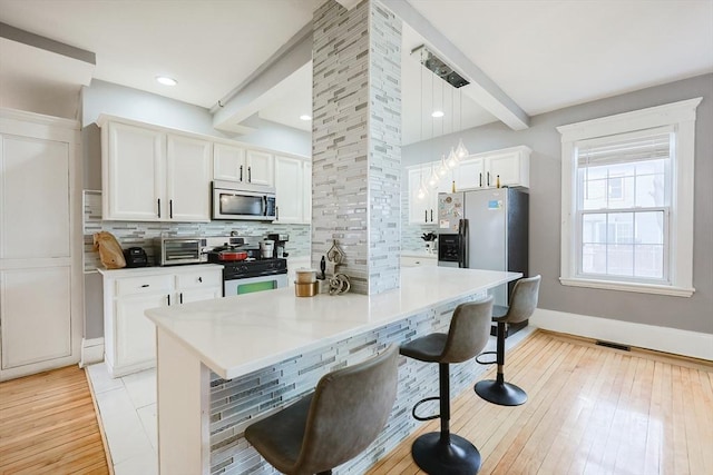 kitchen with beam ceiling, a kitchen breakfast bar, white cabinetry, stainless steel appliances, and decorative backsplash