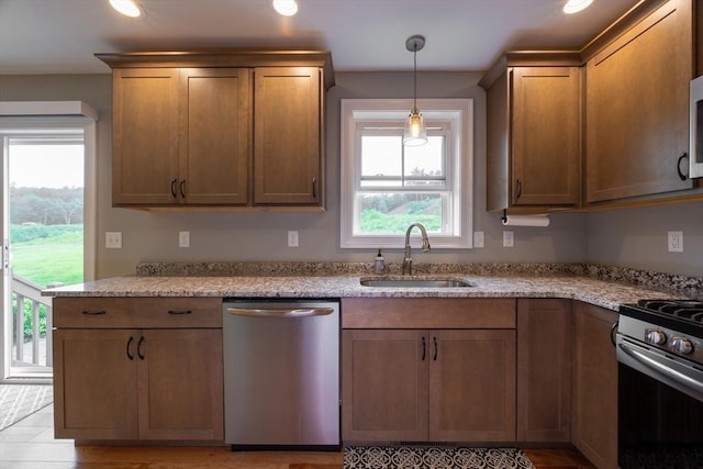 kitchen with light stone countertops, pendant lighting, stainless steel appliances, and sink