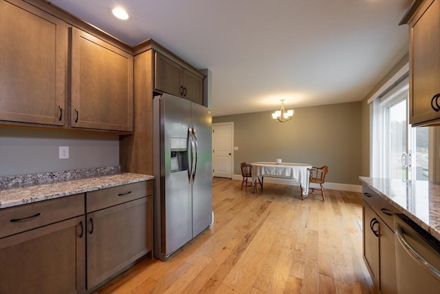 kitchen with light stone countertops, stainless steel appliances, a notable chandelier, light hardwood / wood-style floors, and hanging light fixtures