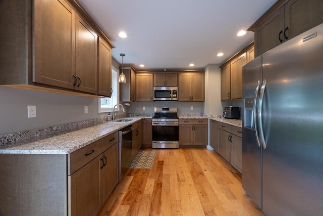 kitchen with pendant lighting, light hardwood / wood-style floors, light stone counters, and stainless steel appliances