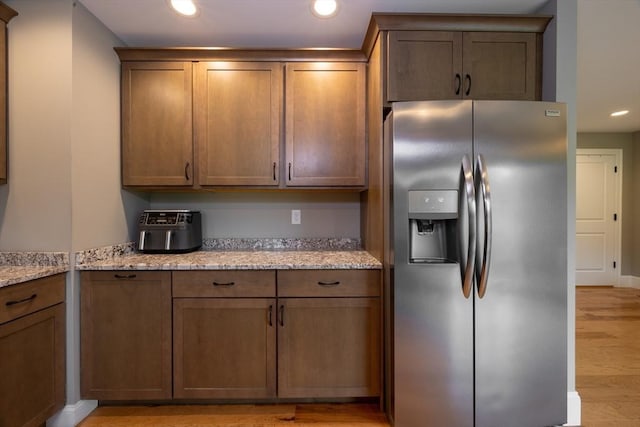 kitchen with stainless steel refrigerator with ice dispenser, light wood-type flooring, and light stone counters