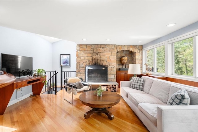 living room with light wood-style floors, a stone fireplace, and recessed lighting