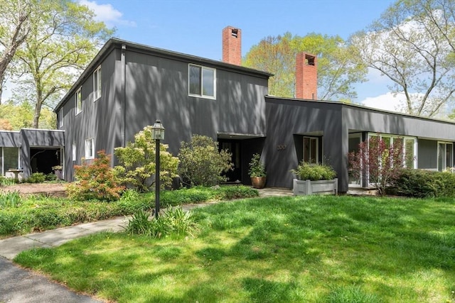 rear view of property featuring a chimney and a lawn