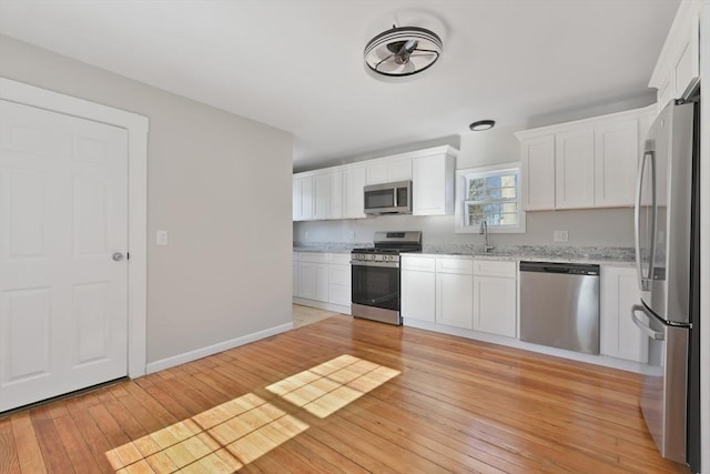 kitchen featuring white cabinetry, light hardwood / wood-style flooring, light stone countertops, and appliances with stainless steel finishes