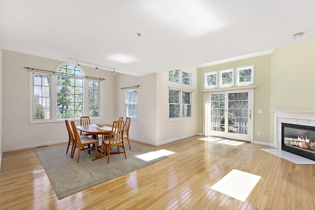 dining area with a tile fireplace, rail lighting, light wood-style floors, and baseboards