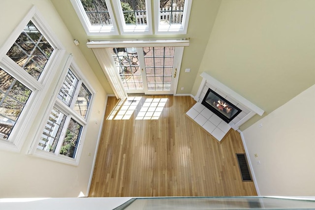 unfurnished living room with baseboards, a glass covered fireplace, visible vents, a towering ceiling, and wood finished floors