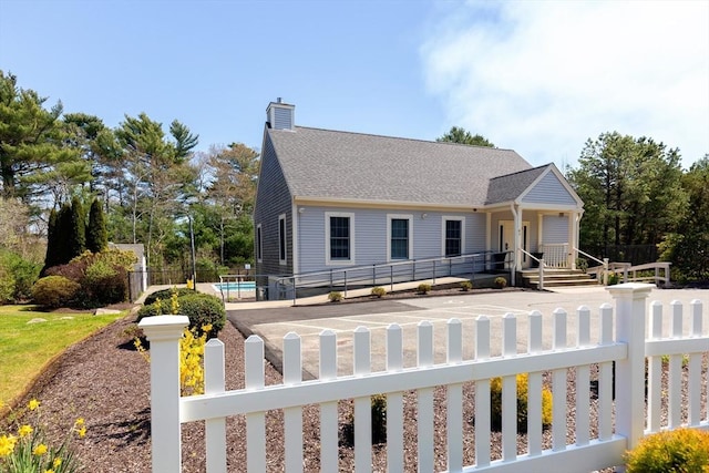 view of front of house with a chimney, a shingled roof, a fenced front yard, and a fenced in pool