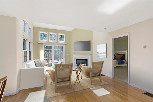 living room featuring a tile fireplace, light wood-type flooring, visible vents, and baseboards
