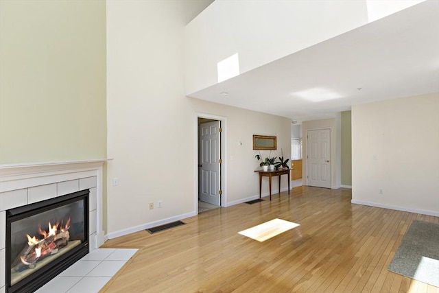 living room with a towering ceiling, visible vents, light wood finished floors, baseboards, and a tiled fireplace