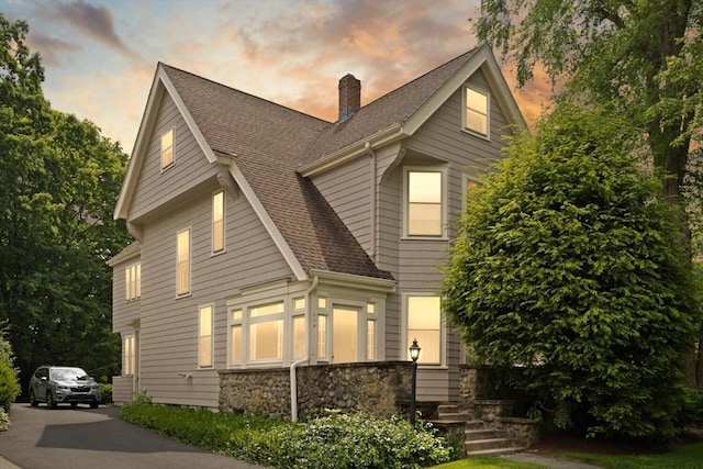 210 Melrose St, Newton, MA 02466 - view of front facade with a shingled roof, a chimney, and stone siding