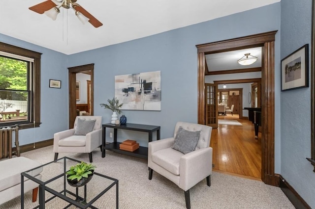living area featuring baseboards, a ceiling fan, and carpet