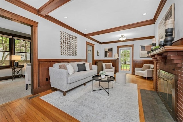 living area featuring a brick fireplace, wainscoting, wood-type flooring, crown molding, and beam ceiling