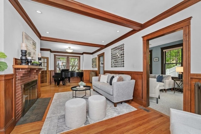 living room featuring a wainscoted wall, ornamental molding, plenty of natural light, a fireplace, and light wood-style flooring