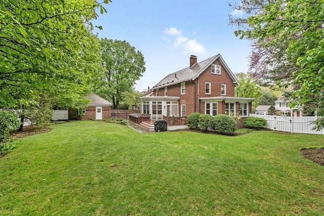 rear view of property featuring a sunroom, brick siding, a chimney, a wooden deck, and an outbuilding