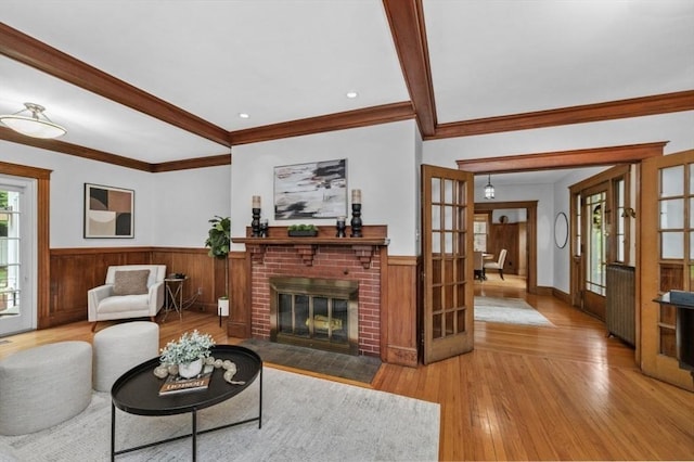 living area with french doors, a wainscoted wall, hardwood / wood-style floors, ornamental molding, and a brick fireplace