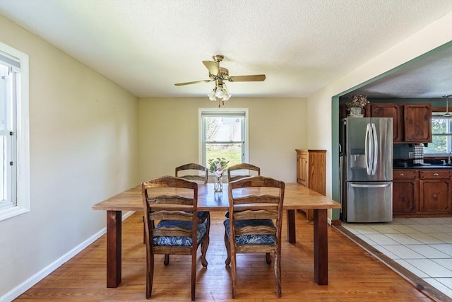 dining room featuring baseboards, ceiling fan, light wood finished floors, and a textured ceiling
