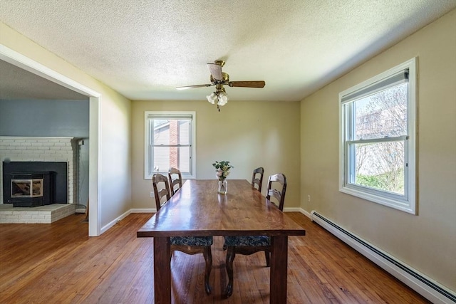 dining space with a textured ceiling, ceiling fan, wood finished floors, and baseboard heating