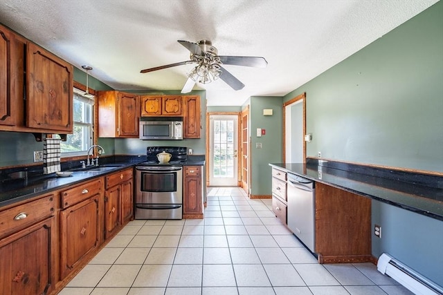 kitchen with brown cabinetry, appliances with stainless steel finishes, dark countertops, a sink, and a baseboard heating unit