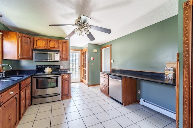 kitchen with brown cabinets, dark countertops, a sink, stainless steel appliances, and a baseboard radiator