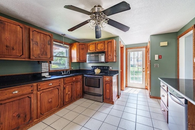 kitchen with a textured ceiling, brown cabinets, a sink, appliances with stainless steel finishes, and light tile patterned floors
