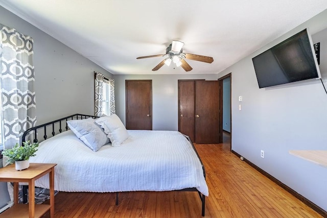 bedroom with light wood-type flooring, multiple closets, ceiling fan, and baseboards