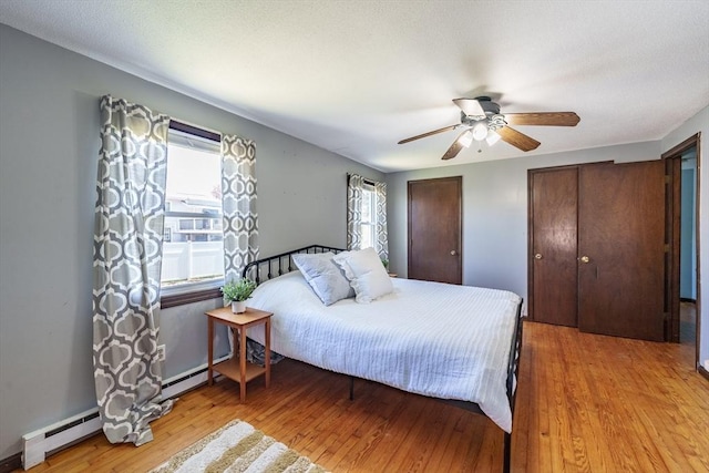 bedroom featuring a baseboard radiator, light wood-style flooring, a ceiling fan, and two closets