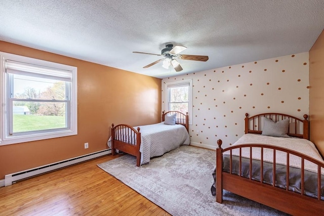 bedroom with a textured ceiling, baseboards, a baseboard heating unit, and light wood-style flooring