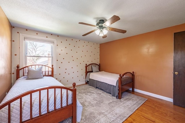 bedroom featuring baseboards, a textured ceiling, light wood finished floors, and ceiling fan