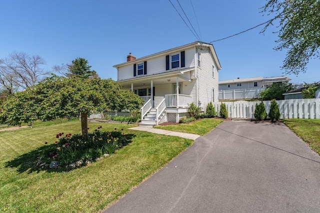 traditional home with a porch, a front lawn, fence, and a chimney
