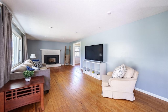 living area featuring wood-type flooring, baseboards, and a brick fireplace