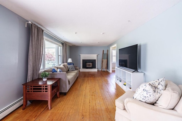 living area with a fireplace, baseboards, a baseboard heating unit, and light wood-type flooring