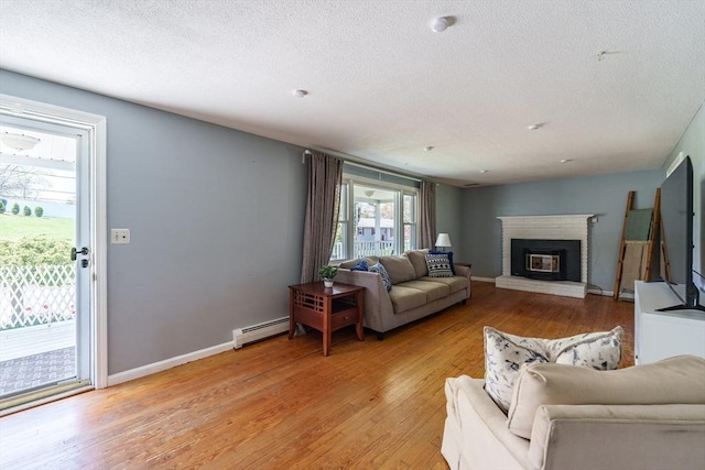 living area featuring light wood-style floors, baseboard heating, a brick fireplace, and a textured ceiling