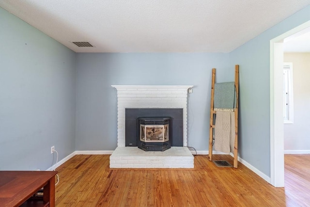 unfurnished living room featuring baseboards, visible vents, wood finished floors, and a wood stove