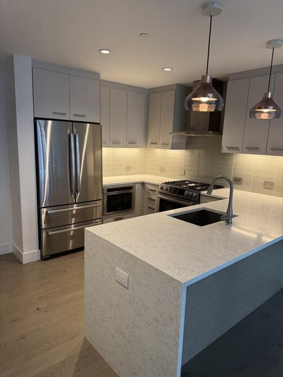 kitchen with sink, wall chimney exhaust hood, stainless steel appliances, kitchen peninsula, and decorative light fixtures