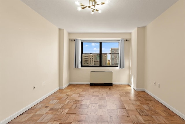 spare room with an inviting chandelier, radiator heating unit, and light parquet floors