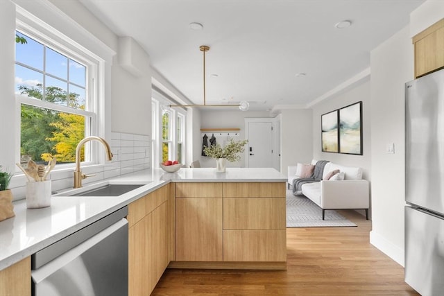 kitchen featuring appliances with stainless steel finishes, sink, backsplash, light brown cabinets, and light hardwood / wood-style flooring