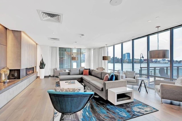 living room with a large fireplace, light wood-style flooring, expansive windows, and visible vents