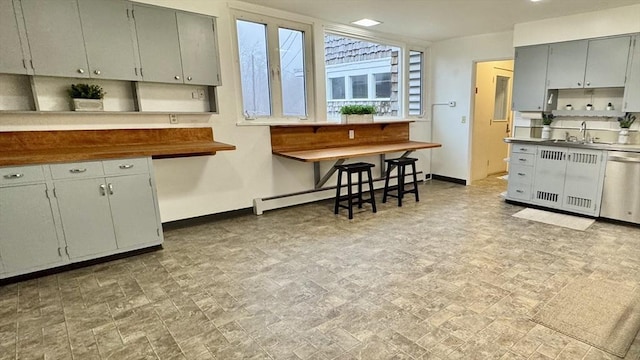 kitchen with butcher block counters, gray cabinetry, sink, stainless steel dishwasher, and a baseboard heating unit