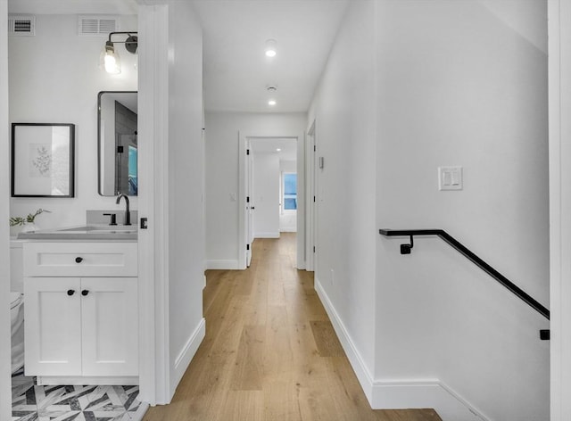 corridor featuring baseboards, visible vents, a sink, and an upstairs landing