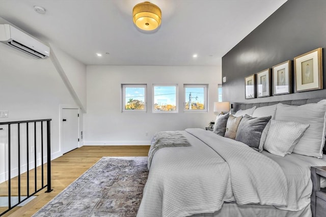 bedroom featuring light wood-style floors, recessed lighting, a wall unit AC, and baseboards