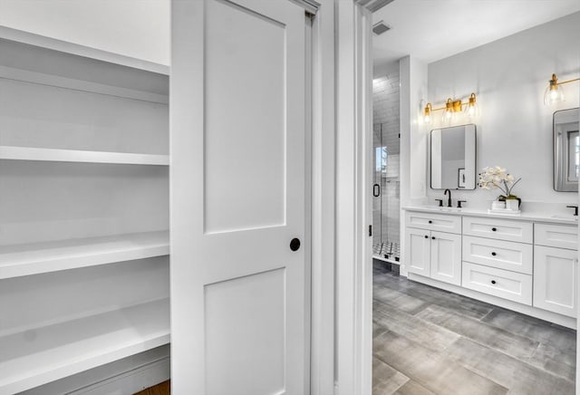 full bathroom featuring double vanity, a shower stall, a sink, and wood finished floors